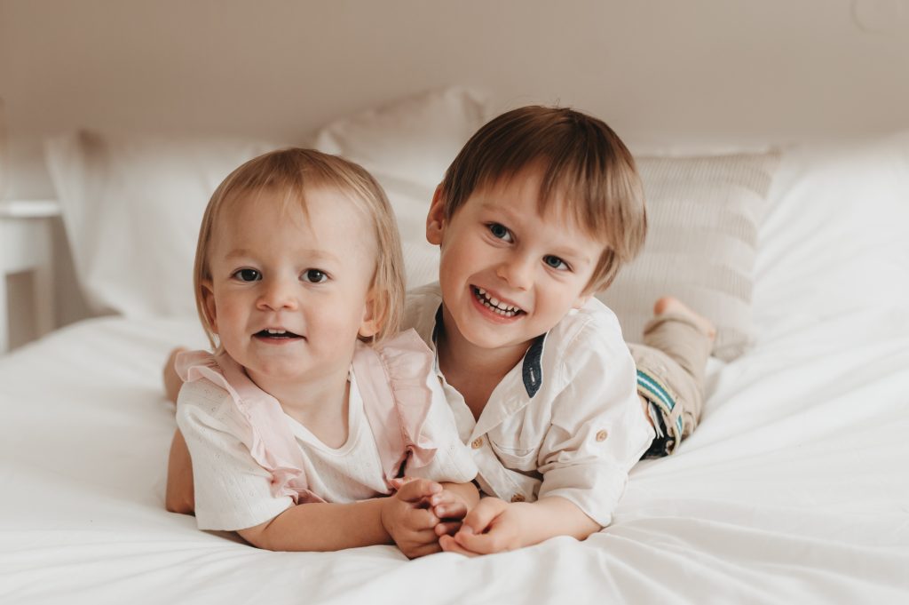 Zwei Geschwister liegen auf einem Bett und lachen
