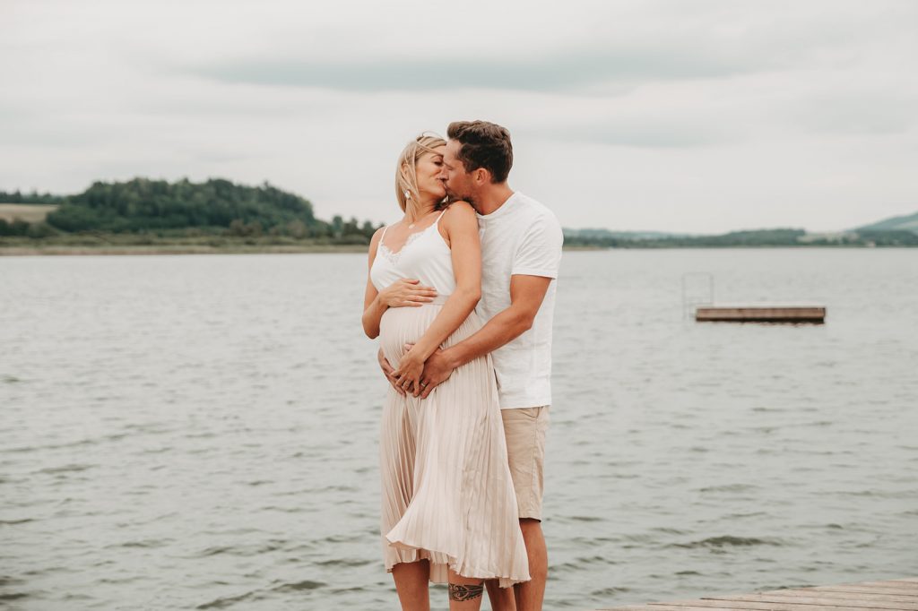 Ein Paar küsst sich am See, Frau ist schwanger, Babybauchfoto